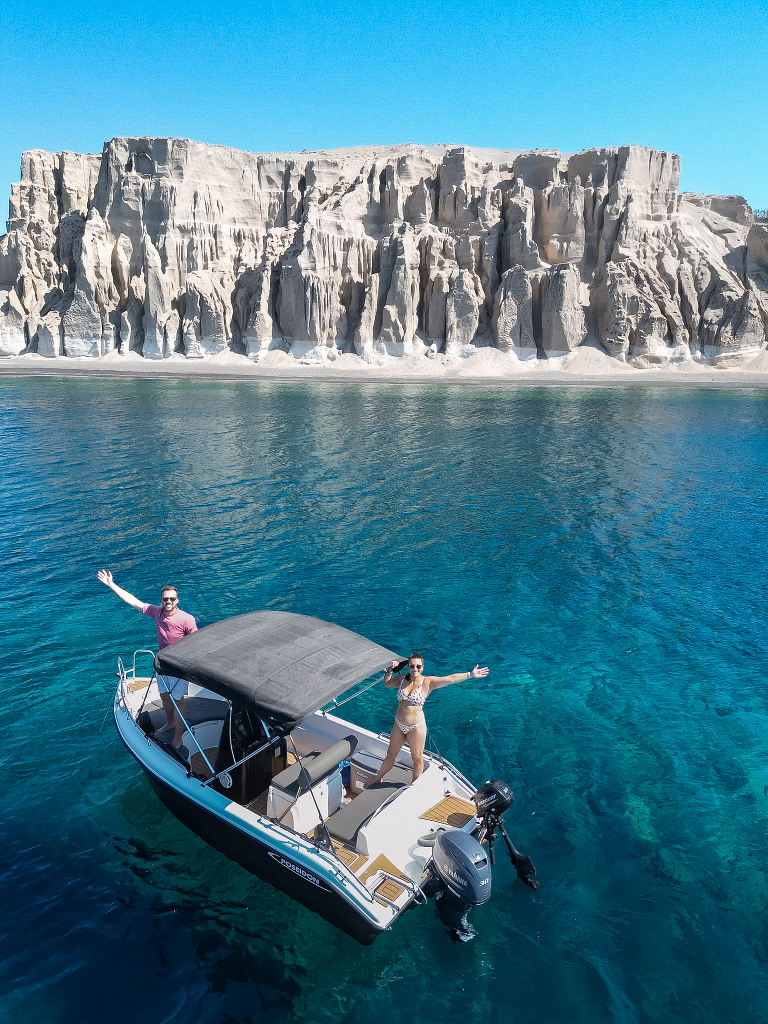 Small self-drive rental boat cruising along Santorini's southern coastline
