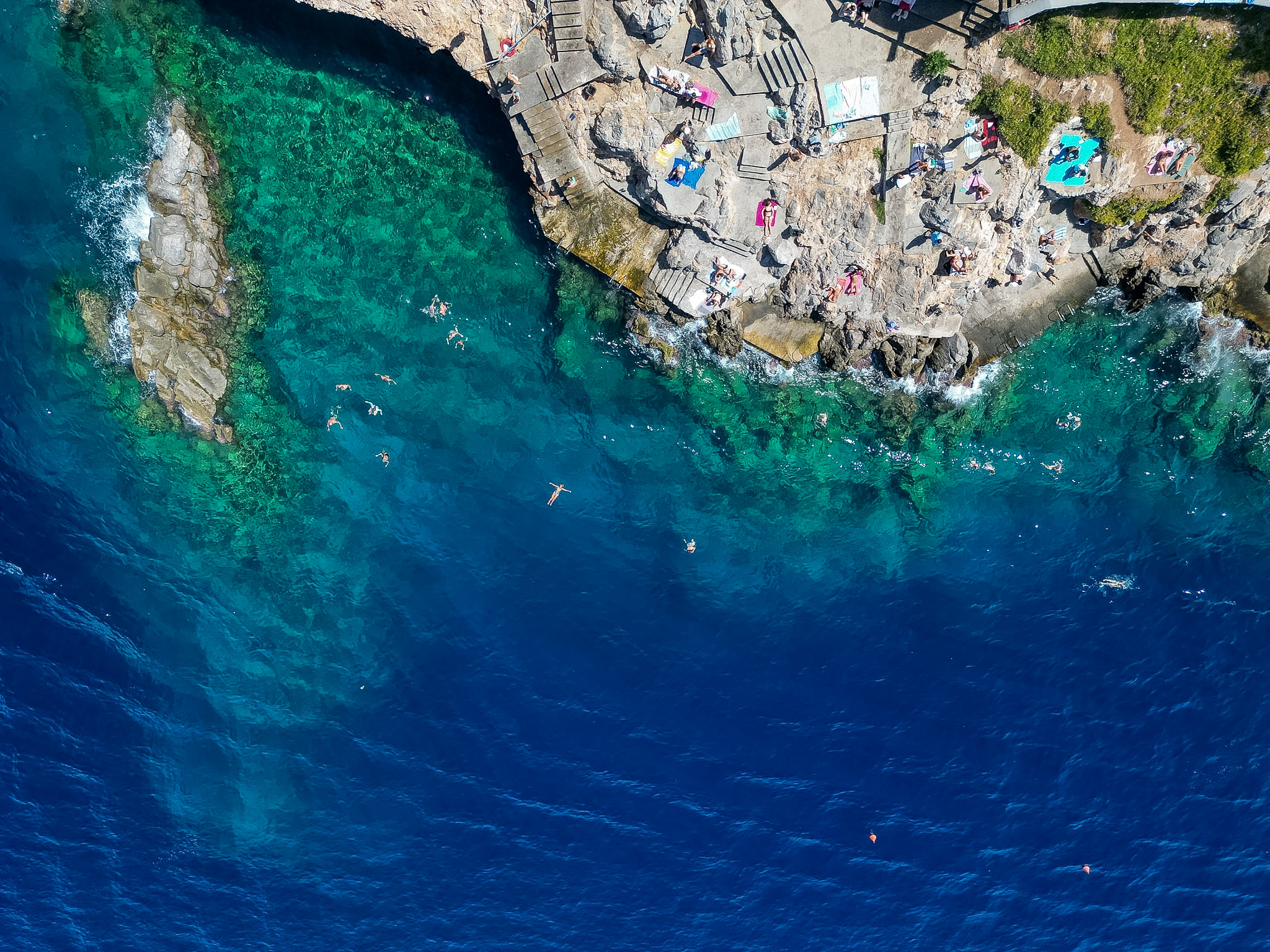 Spilia Beach in Hydra Greece with large flat rocks and clear blue swimming water.